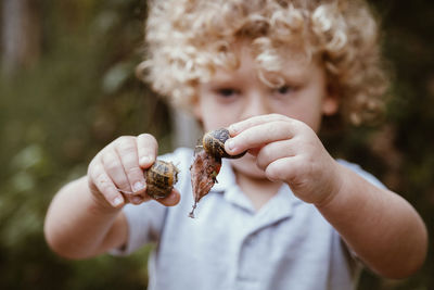 Curious boy holding snails in forest