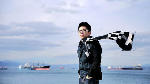 Smiling young man standing by sea against sky