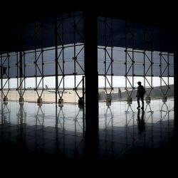 Silhouette man standing at airport against sky seen through window