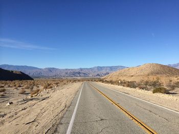 Road leading towards desert against clear blue sky