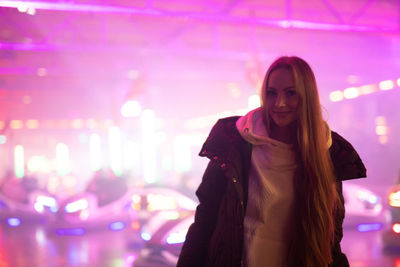 Portrait of smiling young woman standing against illuminated light at night
