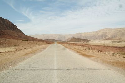 Empty road against mountains against cloudy sky