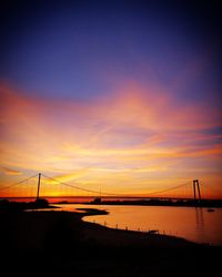 Silhouette bridge over river against sky during sunset