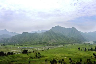 View of green landscape against cloudy sky