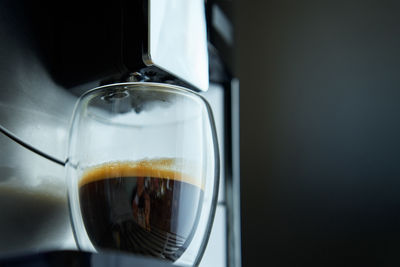 Fresh espresso in clear glass at morning. coffee machine on dark background