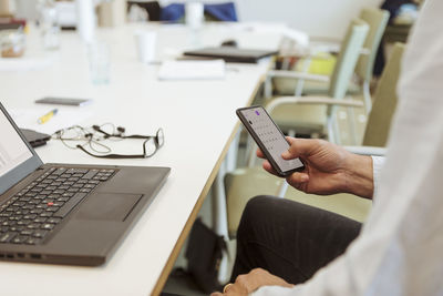 Cropped image of mature businessman using smart phone at conference table in office