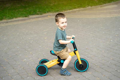A cute toddler boy of two or three years old rides a bicycle or balance bike in a city park