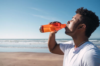 Young man standing at beach against sky