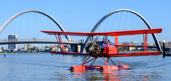 Ferris wheel by river against clear blue sky
