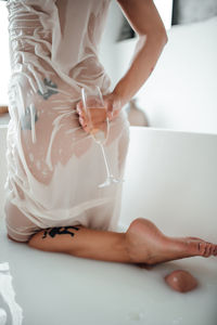 Midsection of woman holding drink in bathtub