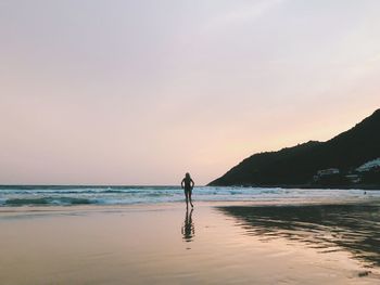 Rear view of woman standing at beach against sky