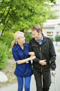 Happy female caretaker walking with disabled senior man on street