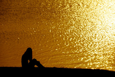 Silhouette man sitting on land against orange sky