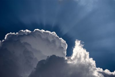 Low angle view of sunlight streaming through clouds