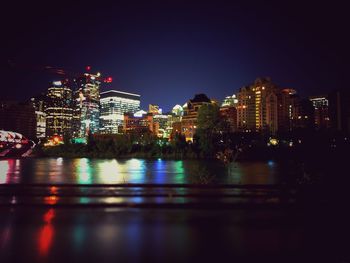 Illuminated city by river against clear sky at night