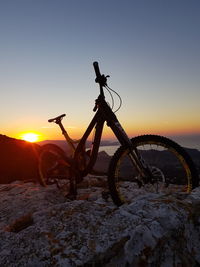 Bicycle on snow covered land against sky during sunset