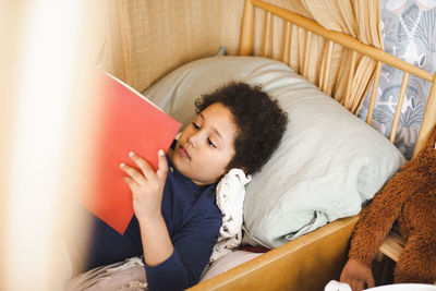 High angle view of boy reading story book while lying on bed at home