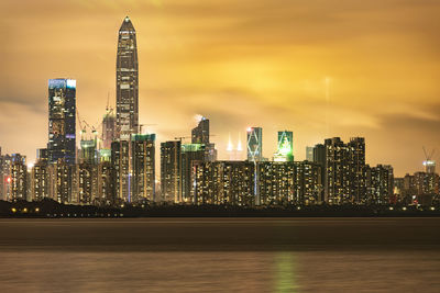 Illuminated modern buildings in city against sky at night