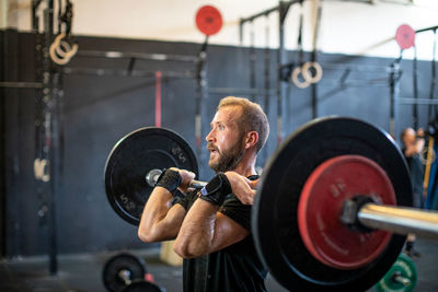 Muscular guy lifting barbell in modern gym