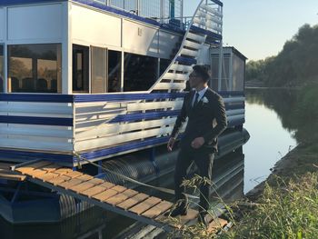 Full length of bridegroom standing on jetty over lake