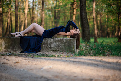 Full length of woman sitting on road in forest