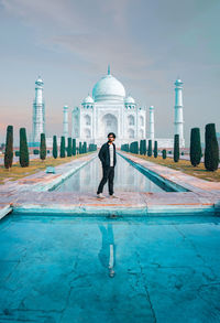 Digital composite image of man standing by swimming pool in building against sky