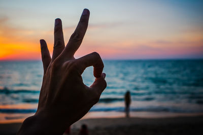 Close-up of hand on beach against sky during sunset