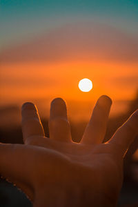 Close-up of hand against sun during sunset