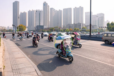 People on road by buildings in city against sky