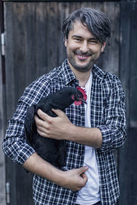 Portrait of happy man carrying hen at poultry farm