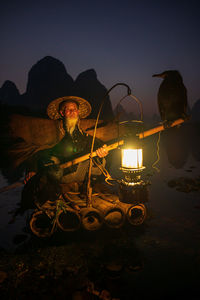 Man sitting in illuminated park against sky at night