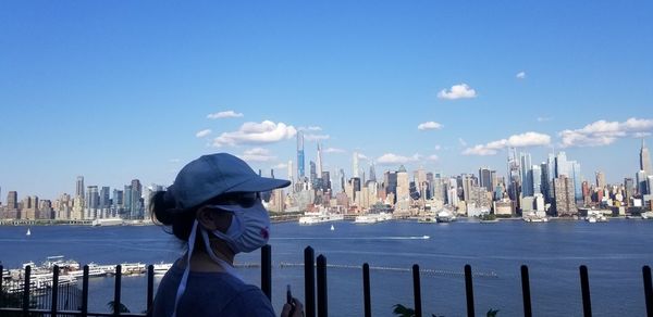 Rear view of woman by sea against buildings in city