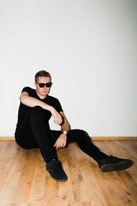 Portrait of young man sitting on hardwood floor against white background