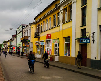 People riding bicycle on road against buildings in city