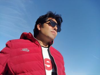 Low angle view of young man looking away against blue sky