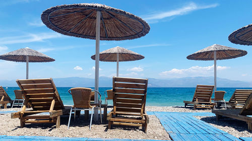 Lounge chairs and tables at beach against sky