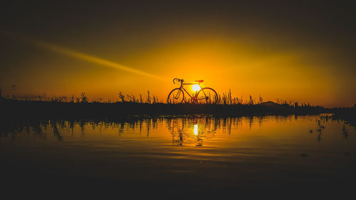 Silhouette plants by lake against sky during sunset