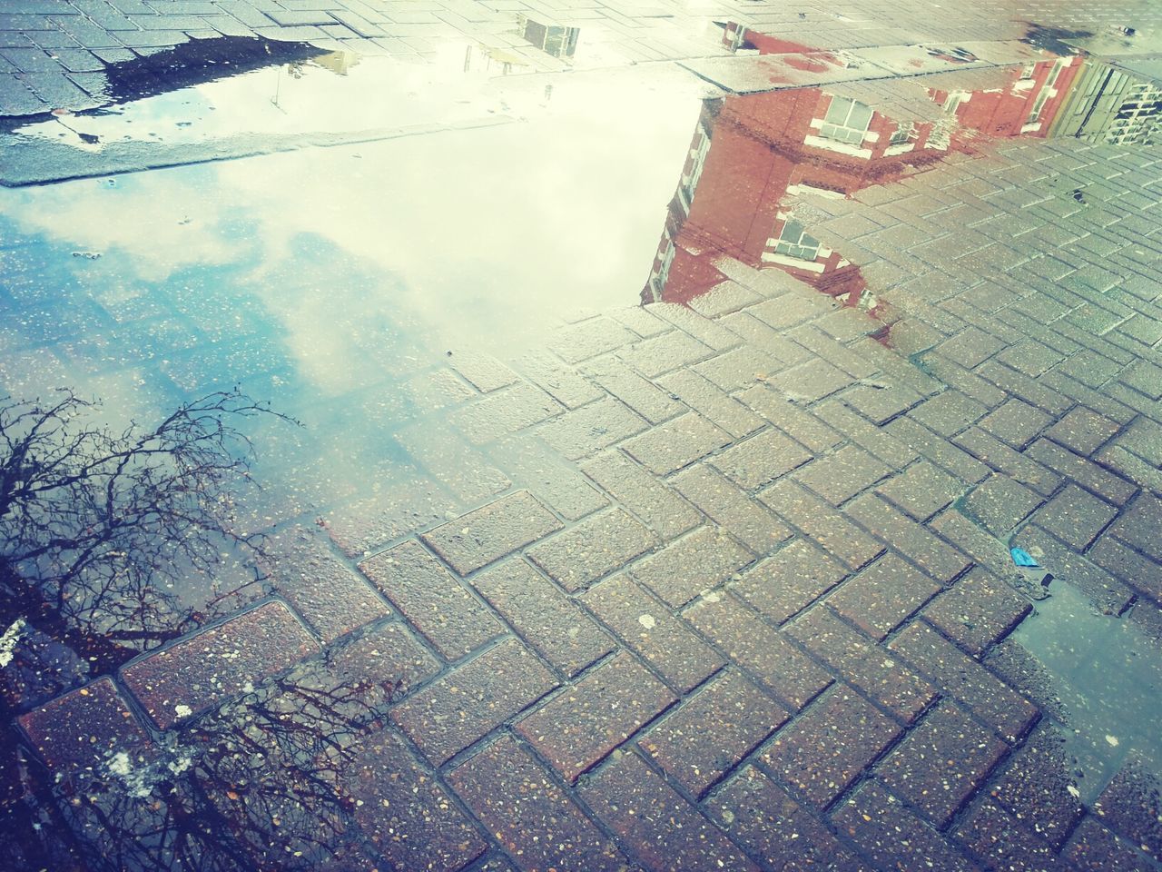 street, high angle view, puddle, building exterior, day, wet, city, rain, cobblestone, outdoors, weather, road, water, built structure, sky, architecture, sidewalk, season, reflection