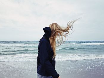 Rear view of woman standing at beach against sky