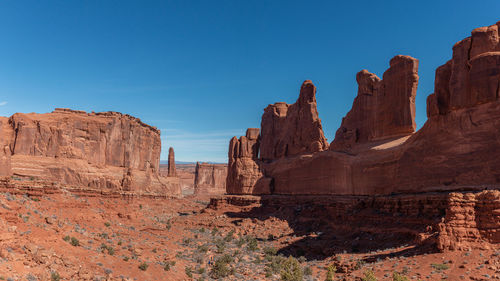 Low angle view of red sandstone rock formations against clear blue sky park avenue area arches park