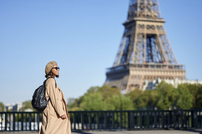 Young woman in trench coat standing by eiffel tower, paris, france