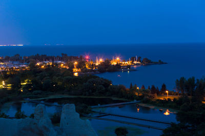 Illuminated city by sea against sky at night