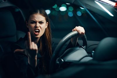Woman showing middle finger sitting in car