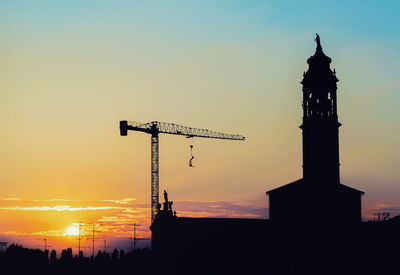 Silhouette cranes in city against sky during sunset
