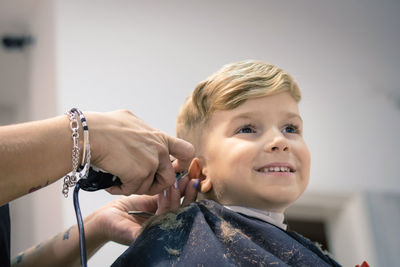 Cropped hands of female barber cutting boy hair in salon