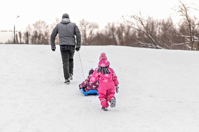 Dad and his two children play and go sledding in the park