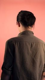 Rear view of young man with hair bun against peach background