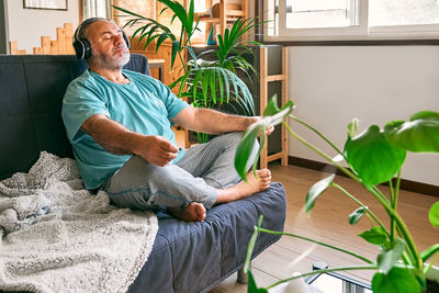 Mature middle-aged overweight man in wireless headphones relaxing at home with guided meditation.