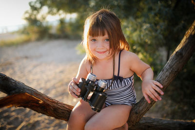 Cute european child girl with binoculars on tree. summer holidays and adventures. jungle  sea coast.