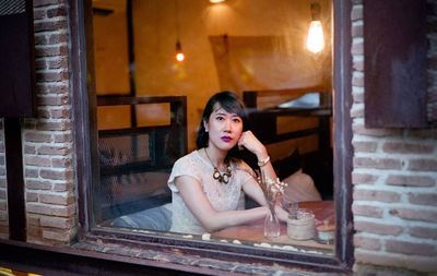 Portrait of young woman sitting on window